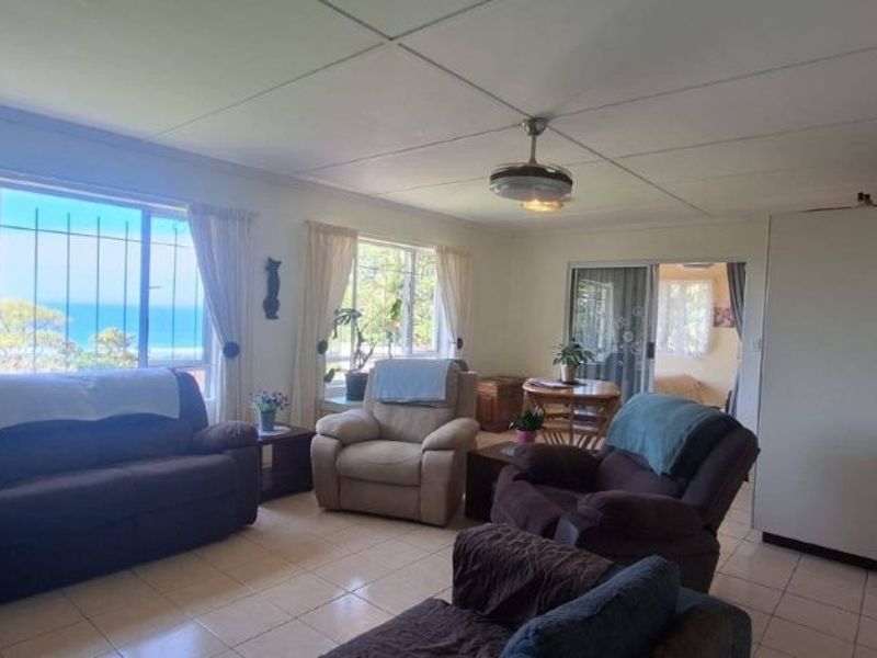 Open-plan living area featuring tiled flooring, a ceiling fan, and large windows with ocean views, seamlessly connecting to the kitchen and adjacent spaces.