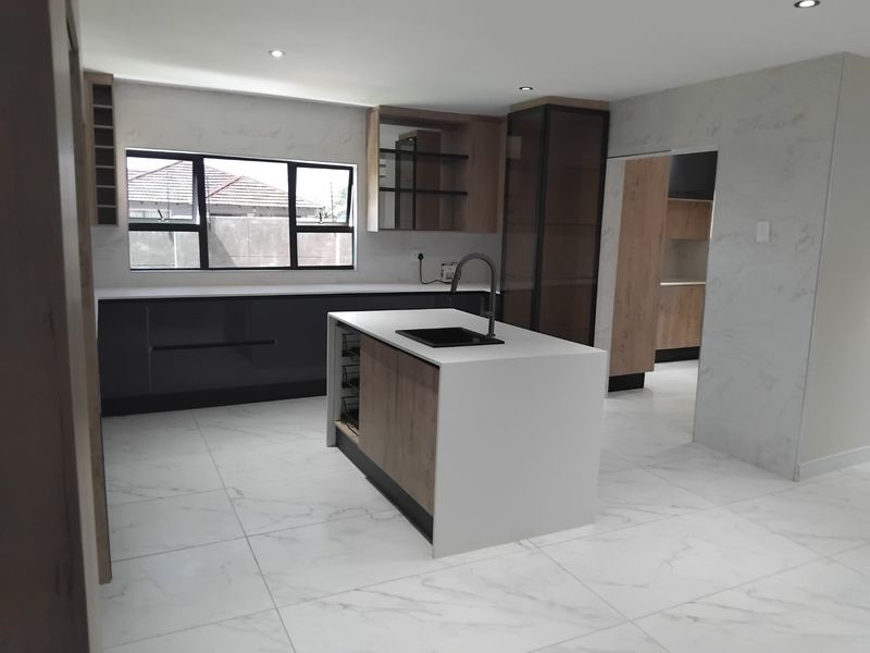 Modern, newly renovated kitchen featuring a central island with quartz countertops, sleek cabinetry, and large-format marble-look floor tiles.