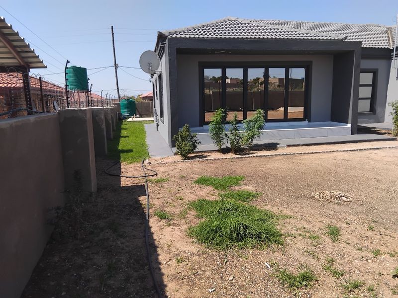 Rear view of the property featuring a tiled roof, modern sliding glass doors, and a perimeter wall with electric fencing and water storage tanks.