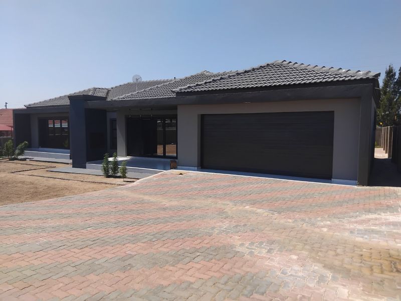Modern single-story house featuring a paved driveway, double garage, and a contemporary facade with a tiled roof and covered entrance.