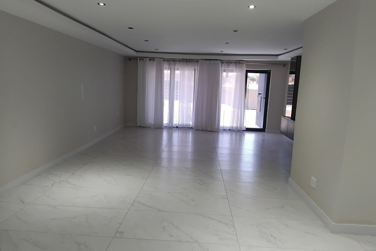 A spacious, empty living area featuring modern white marble-look porcelain tiles, recessed ceiling lighting, and large sliding glass doors leading to the exterior.