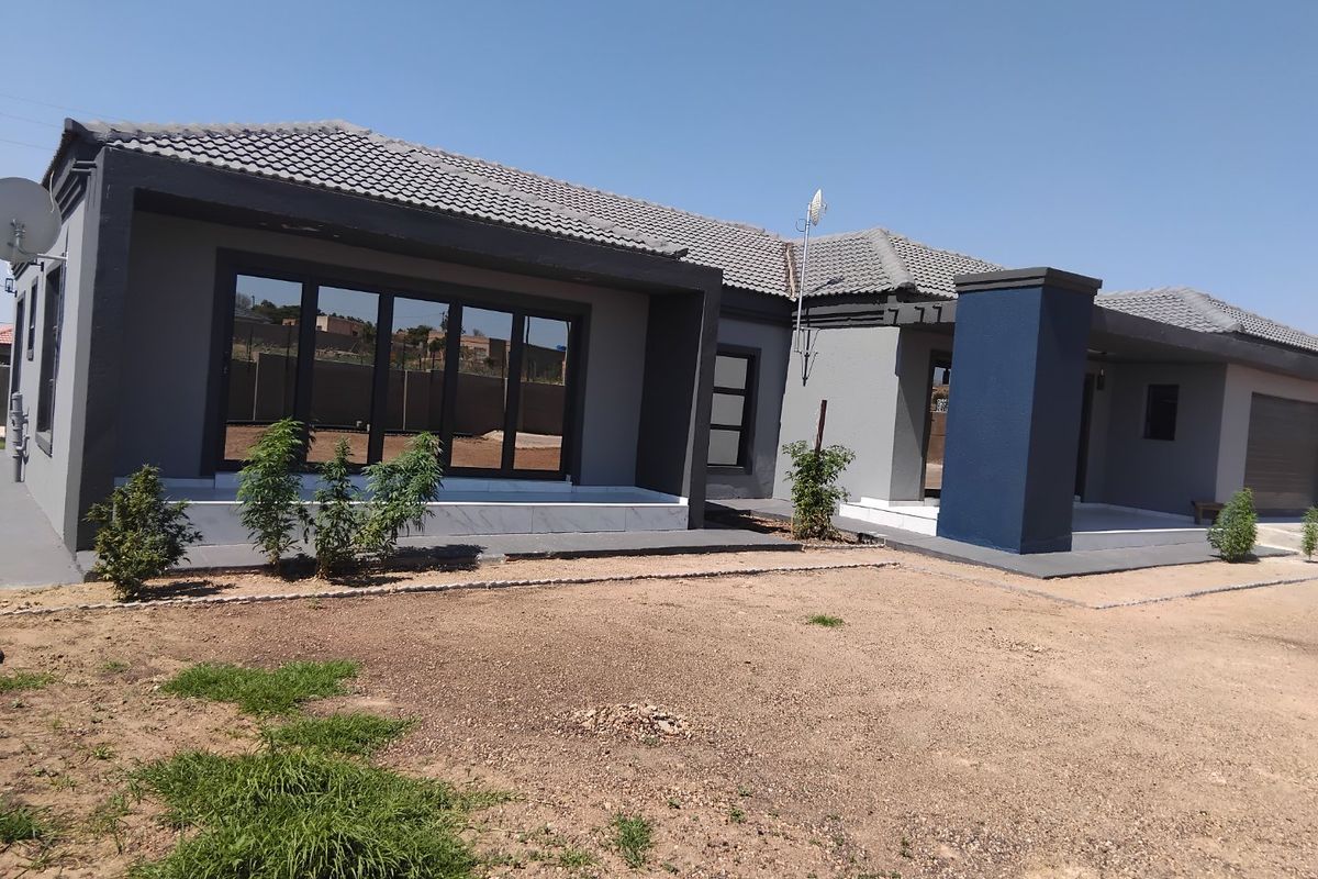 Rear view of a modern single-story house featuring a tiled roof, dark grey and blue exterior paint, and a concrete patio area.