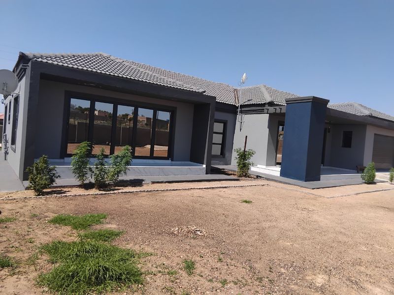 Rear view of a modern single-story house featuring a tiled roof, dark grey and blue exterior paint, and a concrete patio area.