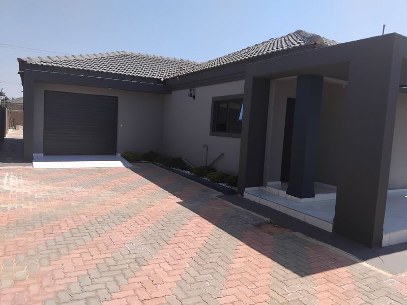 Modern single-story house exterior featuring a paved driveway, integrated garage, and a covered entrance with contemporary dark grey finishes.