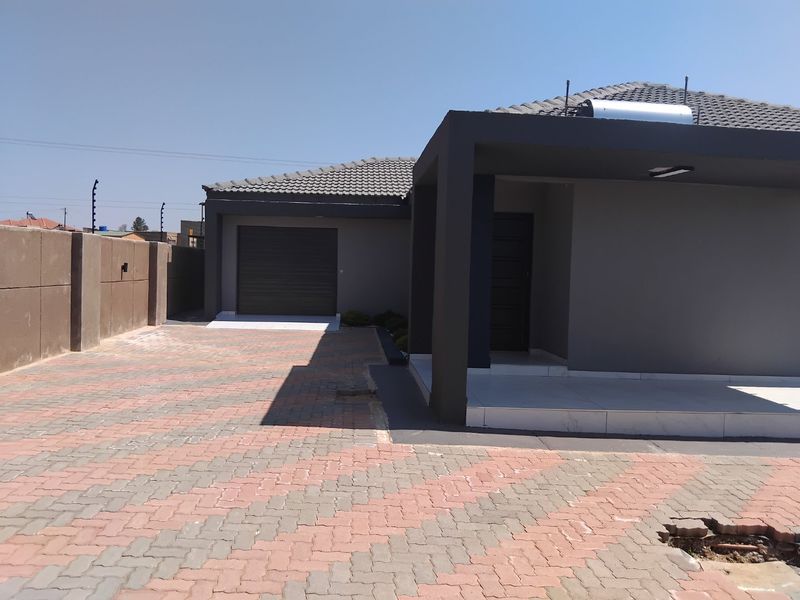 Front view of a modern house featuring a paved driveway, single garage, and a covered entrance with a solar water heater installed on the roof.