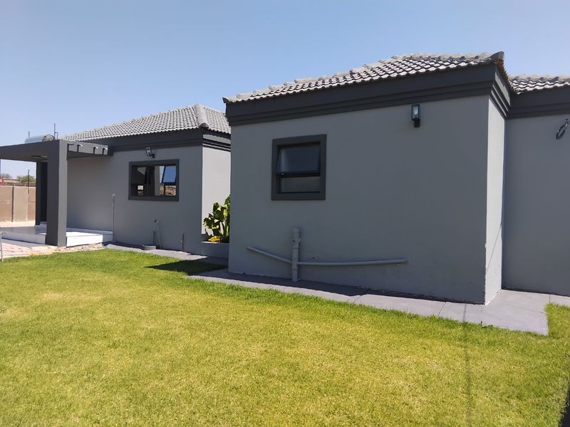 Rear view of the house featuring grey painted exterior walls, tiled roofing, and a well-maintained lawn area.
