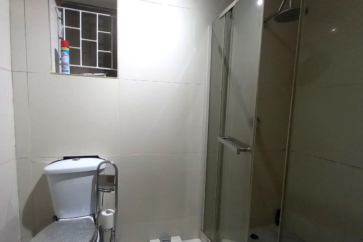 A functional bathroom featuring tiled walls and flooring, a glass shower enclosure, and a standard toilet.