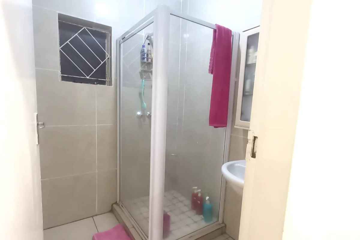 A compact bathroom featuring a glass shower enclosure, wall-mounted basin, and neutral floor-to-ceiling tiling.