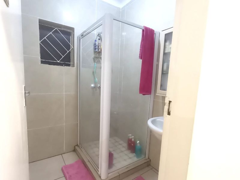A compact bathroom featuring a glass shower enclosure, wall-mounted basin, and neutral floor-to-ceiling tiling.