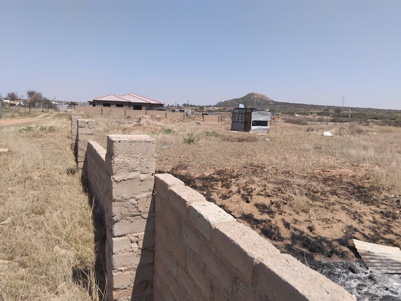 A view of a vacant residential plot featuring a partially constructed concrete block boundary wall and surrounding dry landscape.
