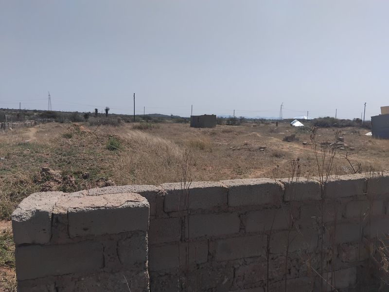 A view of a vacant residential plot featuring a weathered concrete block boundary wall and open, undeveloped land.