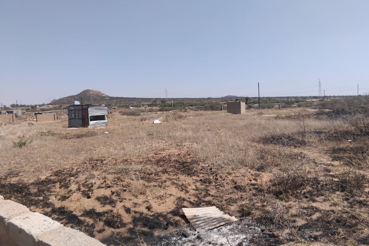 A view of a vacant residential plot featuring dry vegetation and a small temporary structure on the property.