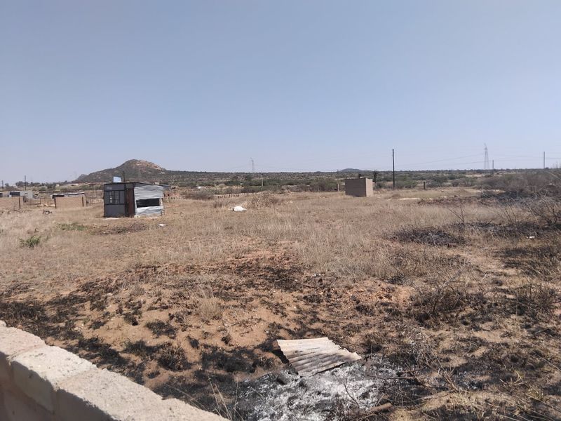 A view of a vacant residential plot featuring dry vegetation and a small temporary structure on the property.