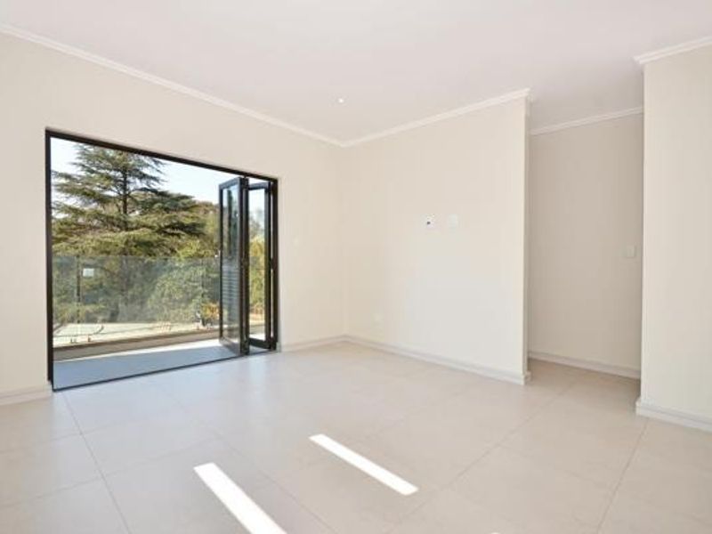 A bright, empty living room featuring large bi-fold doors opening onto a balcony with a glass balustrade and neutral tiled flooring.