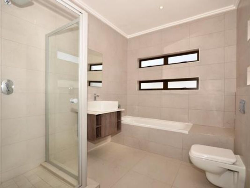 Modern bathroom featuring a glass-enclosed shower, built-in bathtub, wall-hung toilet, and a floating vanity with a vessel sink, finished with neutral wall and floor tiles.
