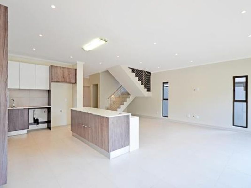 Spacious open-plan living area featuring a modern kitchen with island, tiled flooring, recessed lighting, and a staircase leading to the upper level.