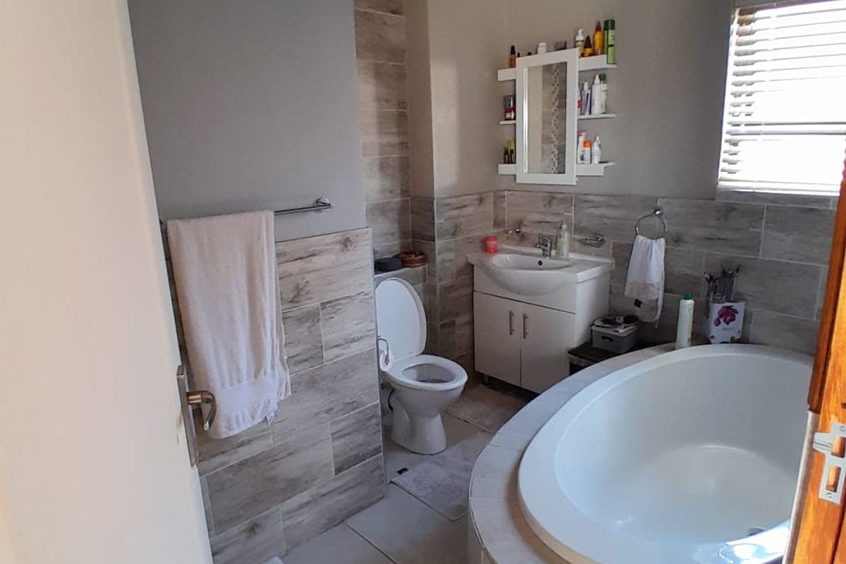 A well-maintained bathroom featuring a built-in bathtub, vanity cabinet with basin, and modern tiled wall finishes with natural light from a window.