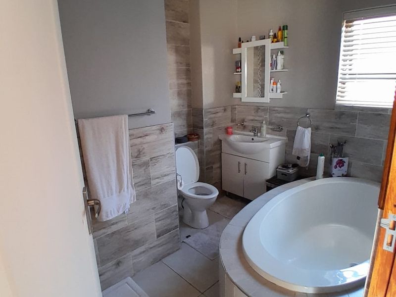 A well-maintained bathroom featuring a built-in bathtub, vanity cabinet with basin, and modern tiled wall finishes with natural light from a window.