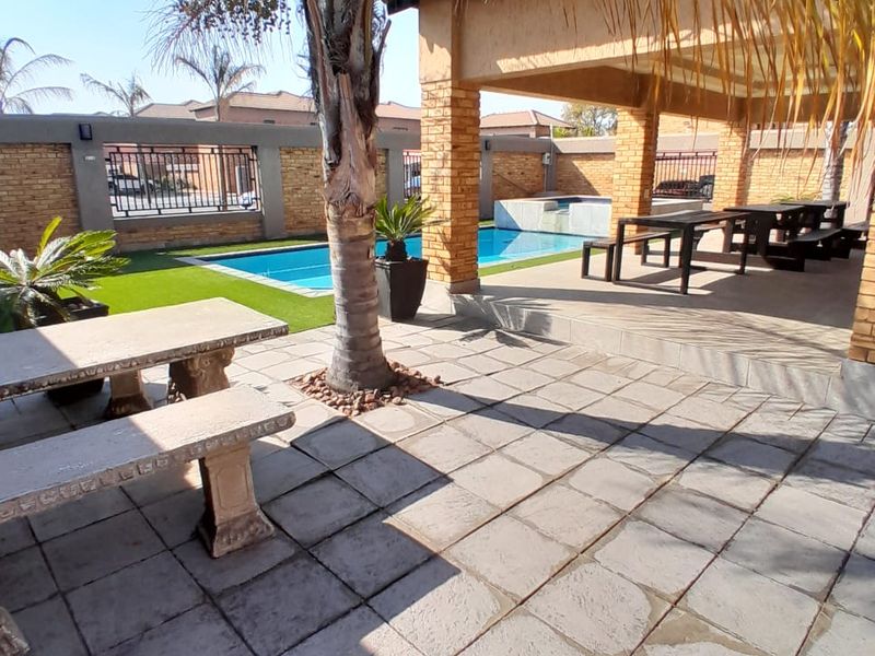 Outdoor entertainment area featuring a covered patio, swimming pool, and paved terrace, enclosed by a secure boundary wall.