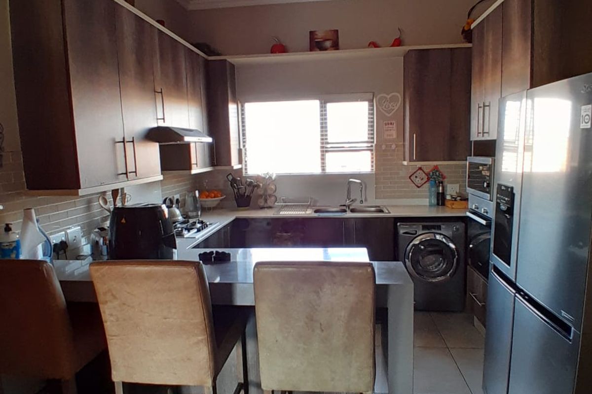 A functional kitchen featuring built-in cabinetry, a breakfast counter, integrated laundry appliances, and tiled flooring with a window providing natural light.