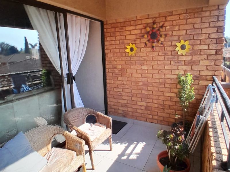 A covered balcony featuring exposed brick walls, tiled flooring, and a sliding glass door providing access to the interior living space.