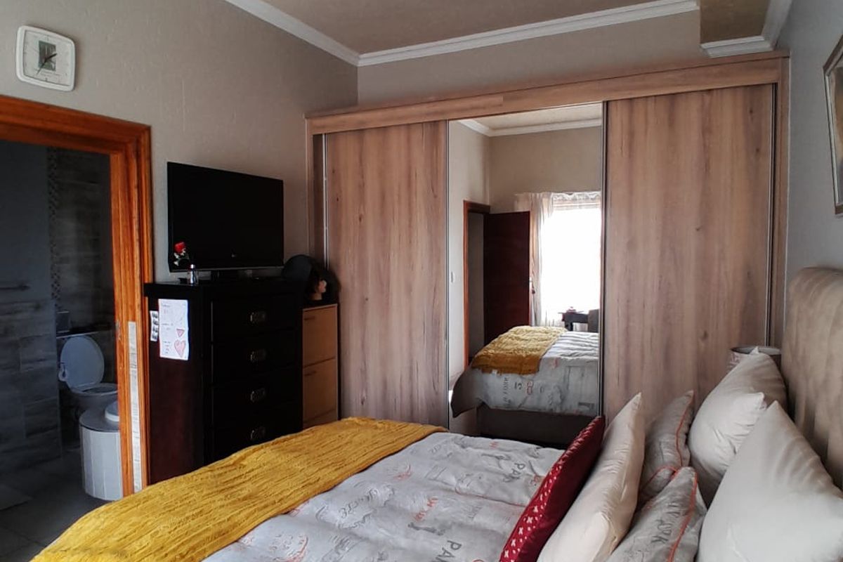 A well-maintained bedroom featuring a large built-in wardrobe with mirrored sliding doors and direct access to an en-suite bathroom.