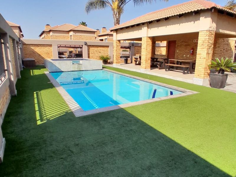 Outdoor pool area featuring a swimming pool, artificial lawn, and a covered patio with stone-clad pillars, ideal for outdoor entertaining.