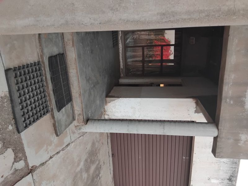 Front entrance area featuring a concrete pillar, roller garage door, and weathered concrete flooring.