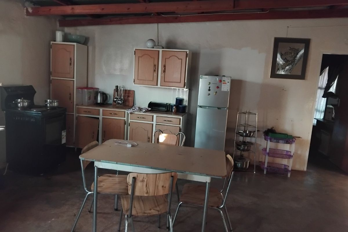 A dated kitchen area featuring basic built-in cabinetry, a freestanding stove, and exposed timber ceiling beams, requiring significant renovation and cosmetic updates.