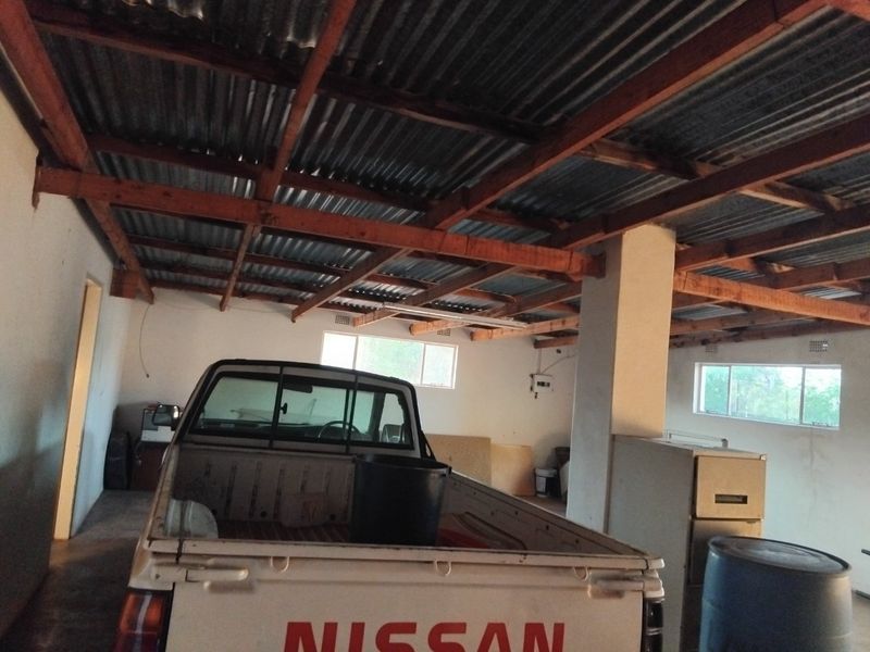A spacious garage featuring exposed timber roof trusses, corrugated metal roofing, and basic electrical infrastructure, providing ample storage or workshop potential.