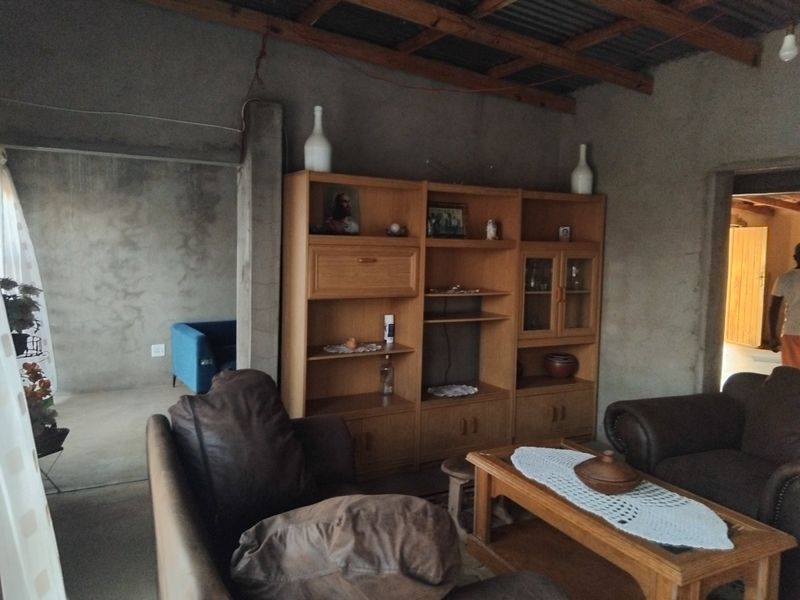 A living room featuring exposed timber roof beams, corrugated metal ceiling, and unfinished cement walls, offering a rustic, industrial-style foundation for renovation.