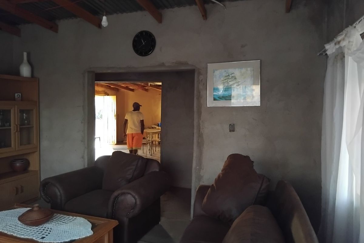 A living room featuring exposed timber rafters, corrugated metal ceiling, and unfinished cement plaster walls, offering a rustic, industrial-style foundation for renovation.