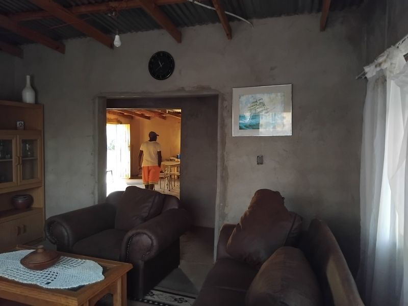 A living room featuring exposed timber rafters, corrugated metal ceiling, and unfinished cement plaster walls, offering a rustic, industrial-style foundation for renovation.