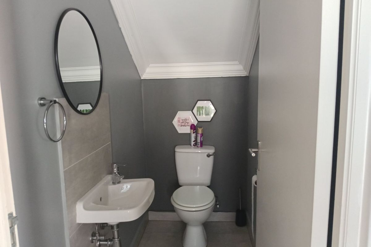 A compact, modern bathroom featuring a wall-mounted basin with chrome mixer, a standard toilet, and neutral grey wall finishes with tiled splashback.
