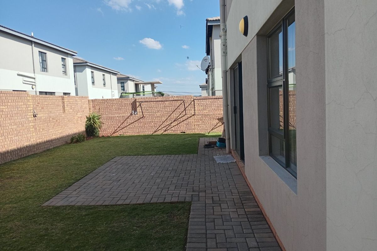 A private rear garden featuring a paved patio area, a well-maintained lawn, and high brick boundary walls for added privacy.