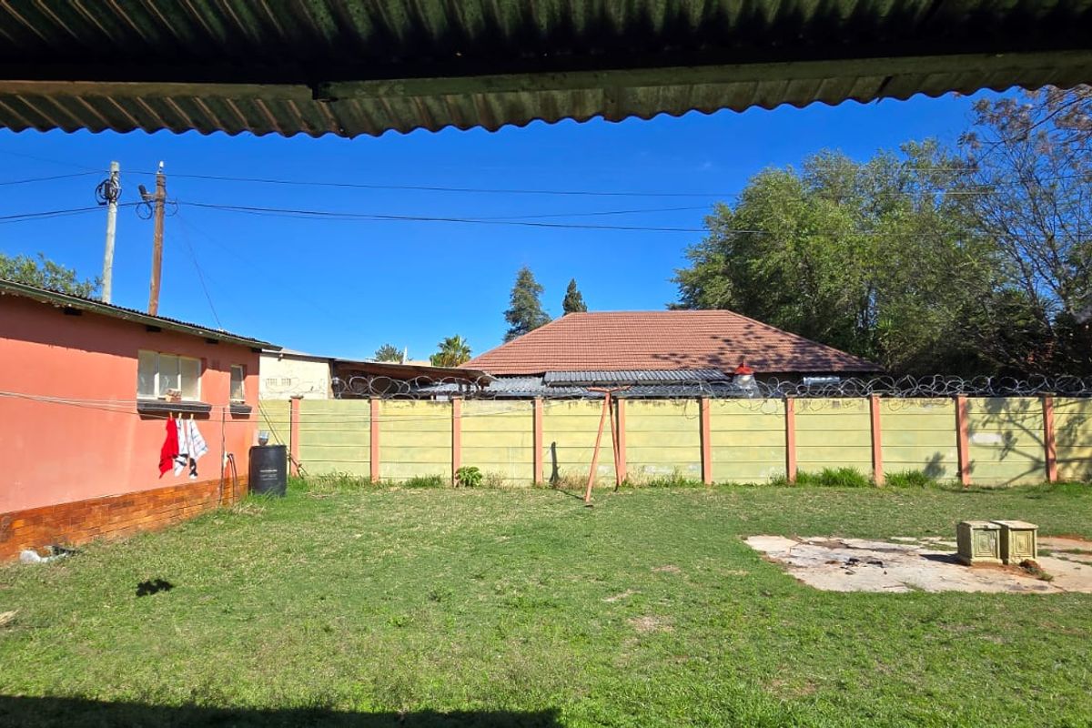 A rear garden area featuring a lawn, a concrete slab, and a precast boundary wall topped with razor wire.