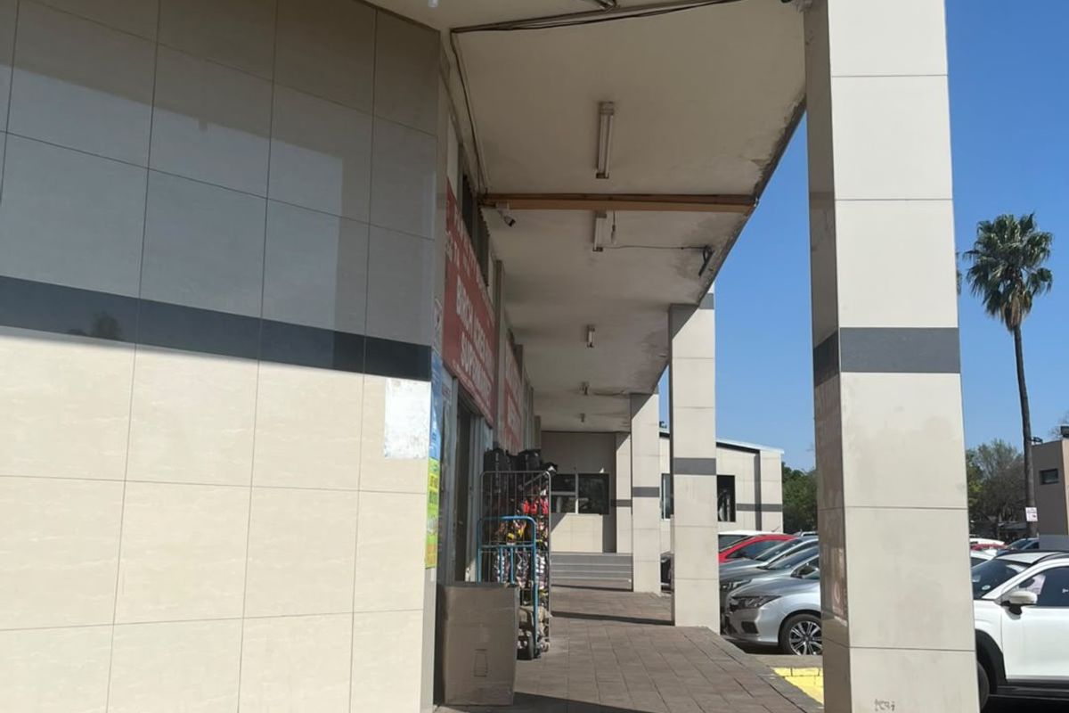 Commercial building exterior featuring a covered walkway, tiled facade, and paved entrance area with visible maintenance required on the ceiling soffit.