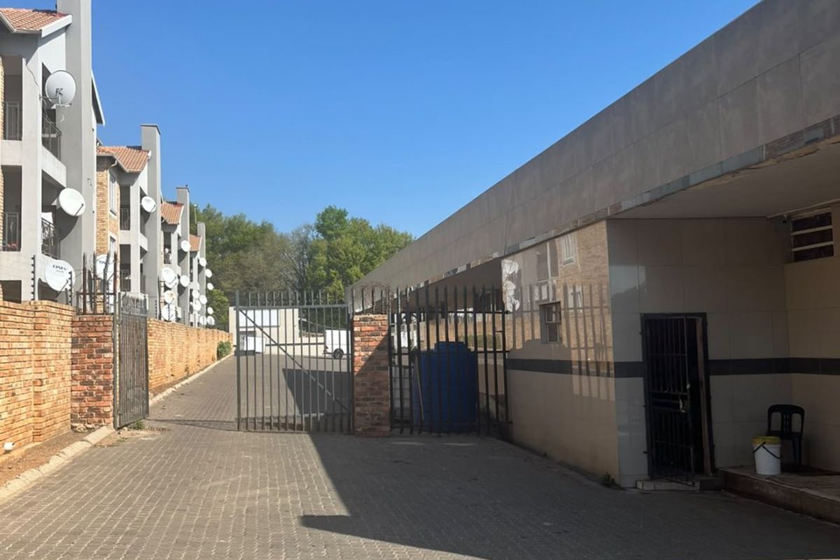 A paved driveway leading to a secure gated entrance of a commercial property, featuring brick boundary walls and a tiled building facade.