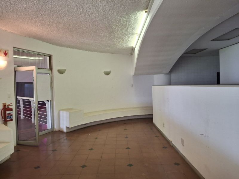 Spacious commercial hallway featuring tiled flooring, a curved built-in bench, and textured ceiling finishes, providing a functional transition area within the property.
