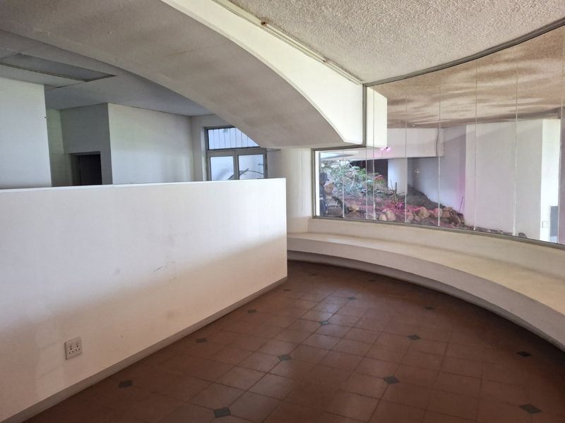 Spacious interior area featuring a unique curved built-in bench, large windows with garden views, and tiled flooring, offering a versatile layout for commercial use.