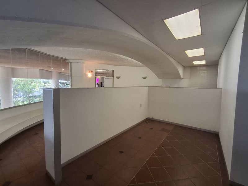 An open-plan commercial space featuring a distinctive curved architectural archway, recessed ceiling lighting, and large glass windows providing natural light.
