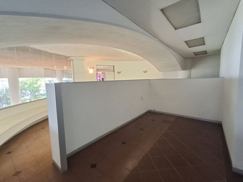An open-plan commercial space featuring a unique curved ceiling, tiled flooring, and large windows providing natural light, suitable for various office or retail configurations.