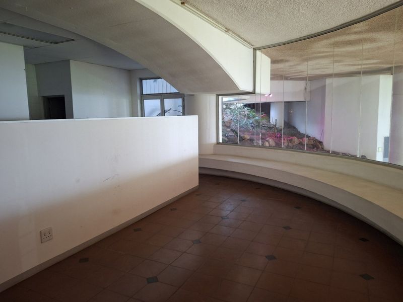 An open-plan commercial space featuring a unique curved built-in bench, large windows overlooking an outdoor area, and tiled flooring throughout.