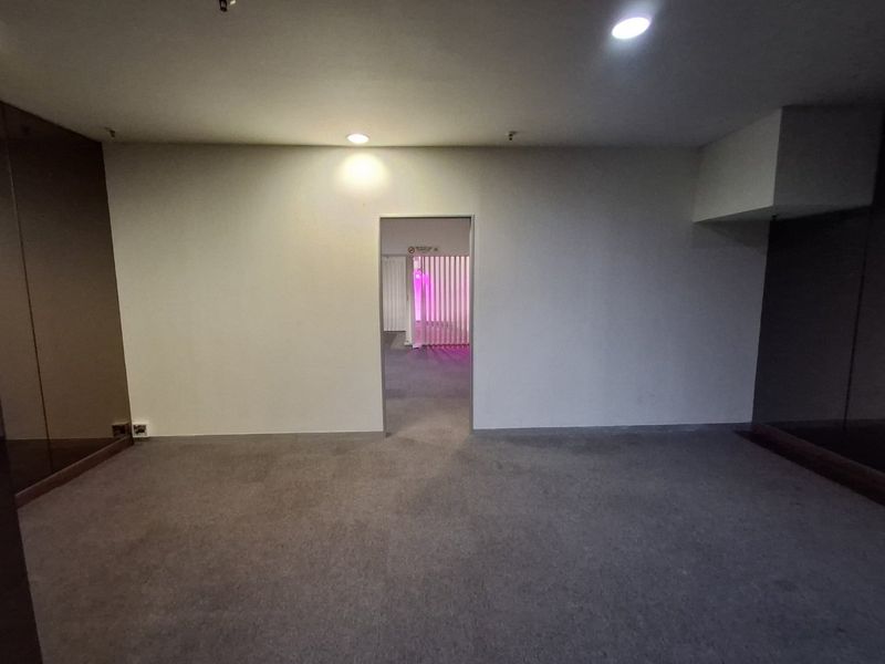 A vacant commercial hallway featuring neutral carpeting, recessed ceiling lighting, and a central doorway leading to an adjacent space.