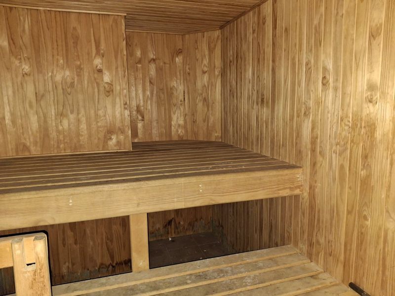 A dedicated sauna room featuring timber wall paneling and built-in wooden bench seating, showing signs of wear and moisture exposure.