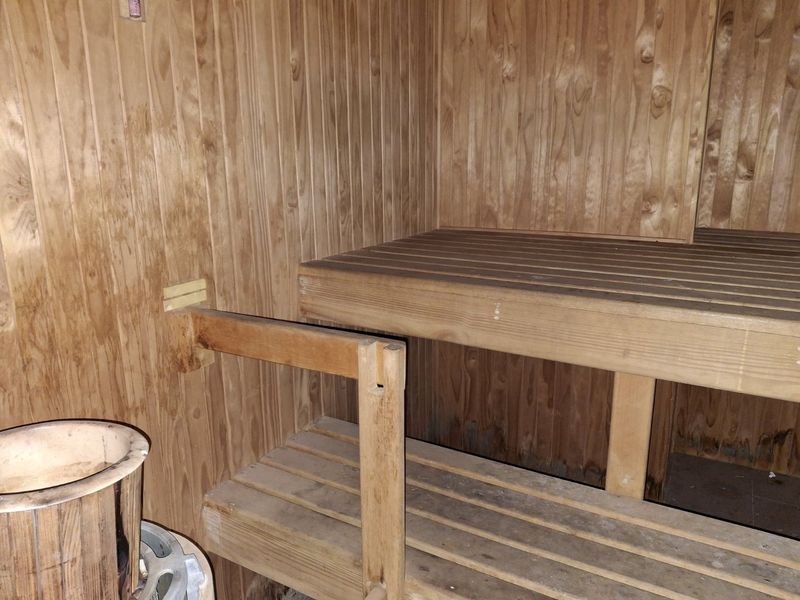 A compact sauna featuring traditional timber wall paneling and built-in wooden bench seating, showing signs of age and wear.