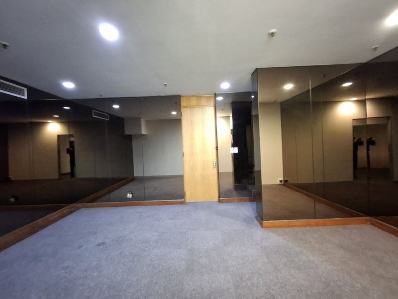 An empty commercial office space featuring mirrored wall panels, recessed lighting, and carpet flooring, suitable for a variety of professional business uses.