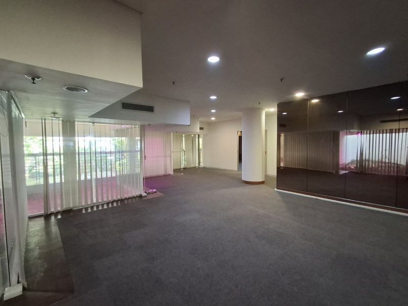Spacious open-plan commercial office area featuring recessed lighting, central air conditioning, mirrored wall accents, and large windows with vertical blinds.