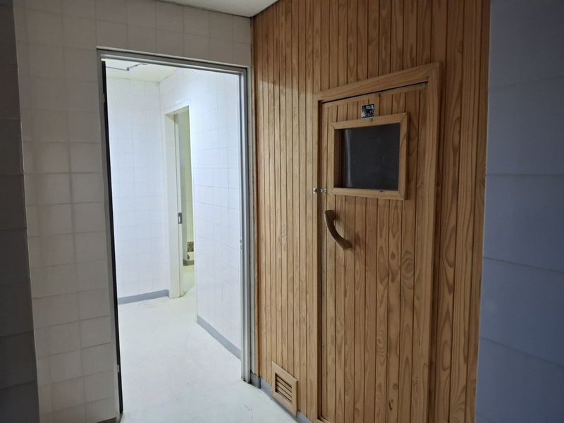 A dedicated sauna room featuring timber wall paneling and a wooden door, adjacent to a tiled hallway area.