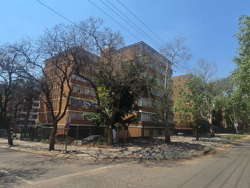 Street view of a multi-story brick apartment complex featuring perimeter fencing and mature trees in a residential neighborhood setting.